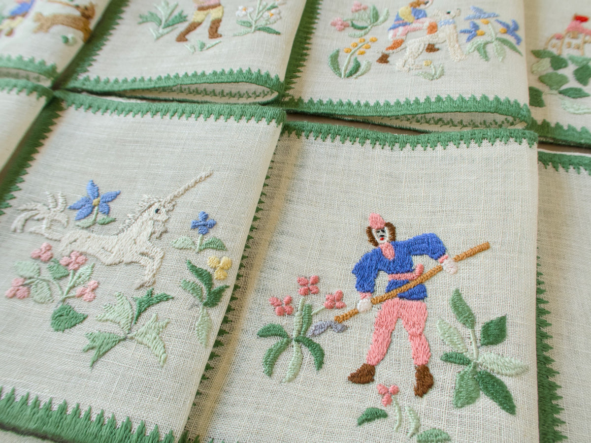 Close-up of two vintage Baroness Rapisardi  cocktail napkins showing a running unicorn among blue and pink flowers beside a hunter in a blue jacket and pink trousers holding a long lance
