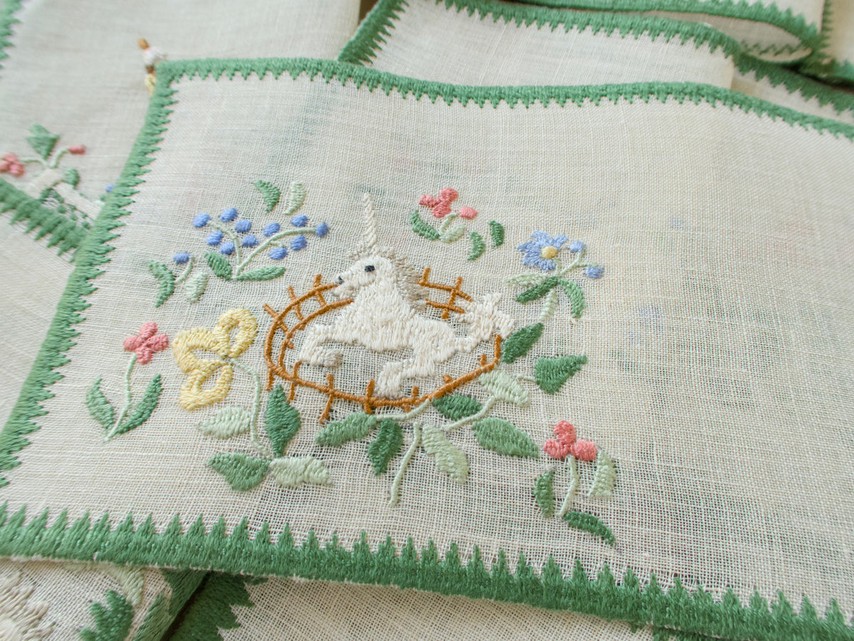 Closeup of a vintage Baroness Rapisardi cocktail napkin opened flat to show the semi-sheer linen, showing a hand embroidered unicorn in a golden fence.