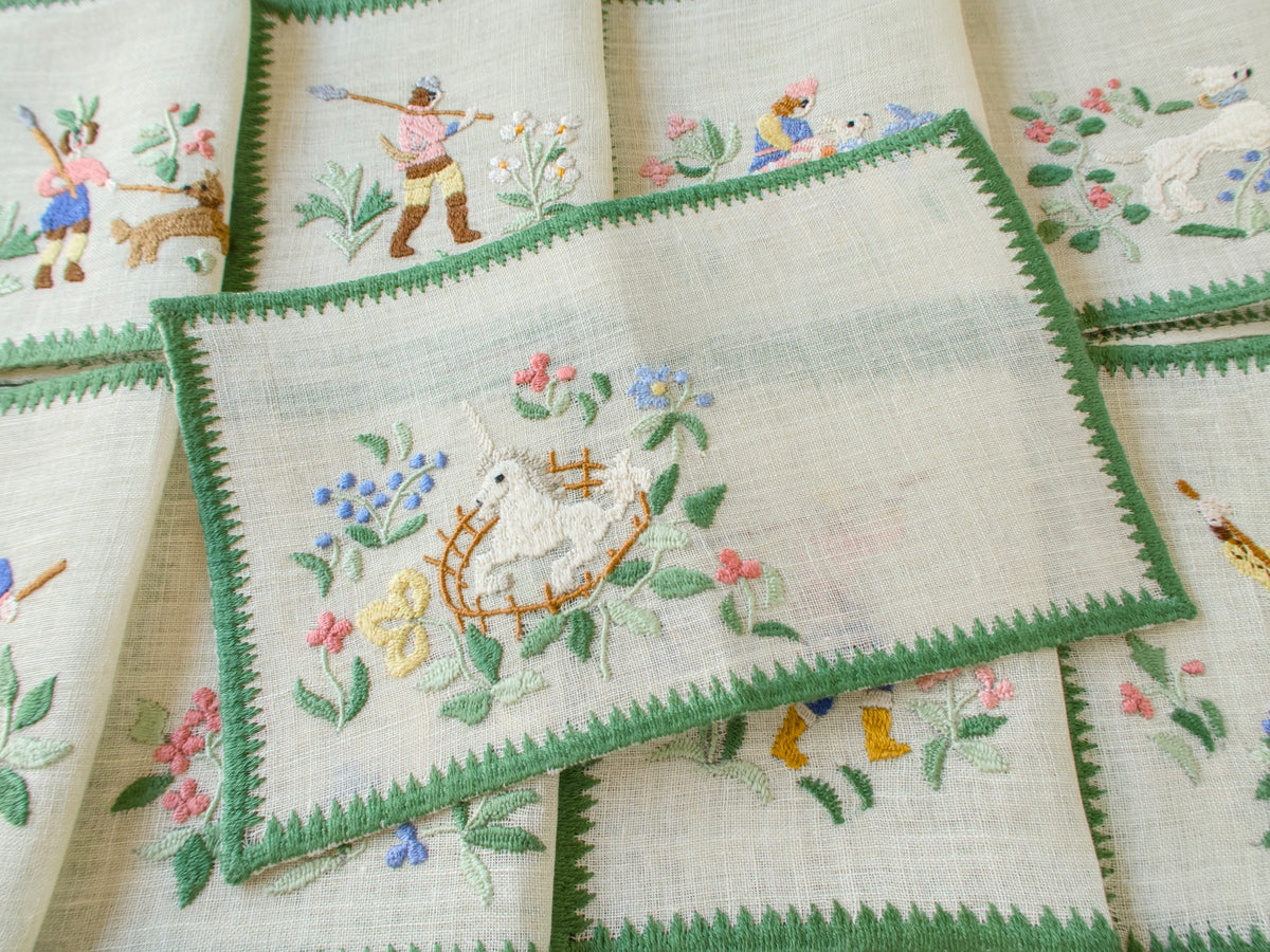 Baroness Rapisardi vintage cocktail napkin opened flat to show the semi-sheer linen, with the unicorn in a golden fence embroidered at one end and hunter napkins folded behind it