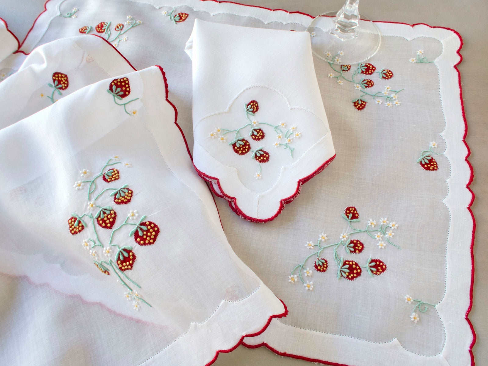 Vintage Madeira linen napkin on organdy placemat showing red strawberry embroidery detail and edge of organdy runner with red scalloped border