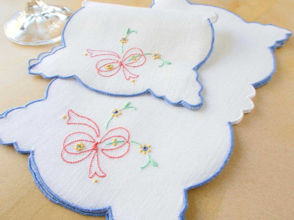 Vintage Madeira linen cocktail napkins hand embroidered with pink ribbon bows and scattered yellow and blue posies, cut in a graceful sculpted silhouette with blue scalloped edges​​​​​​​​​​​​​​​​
