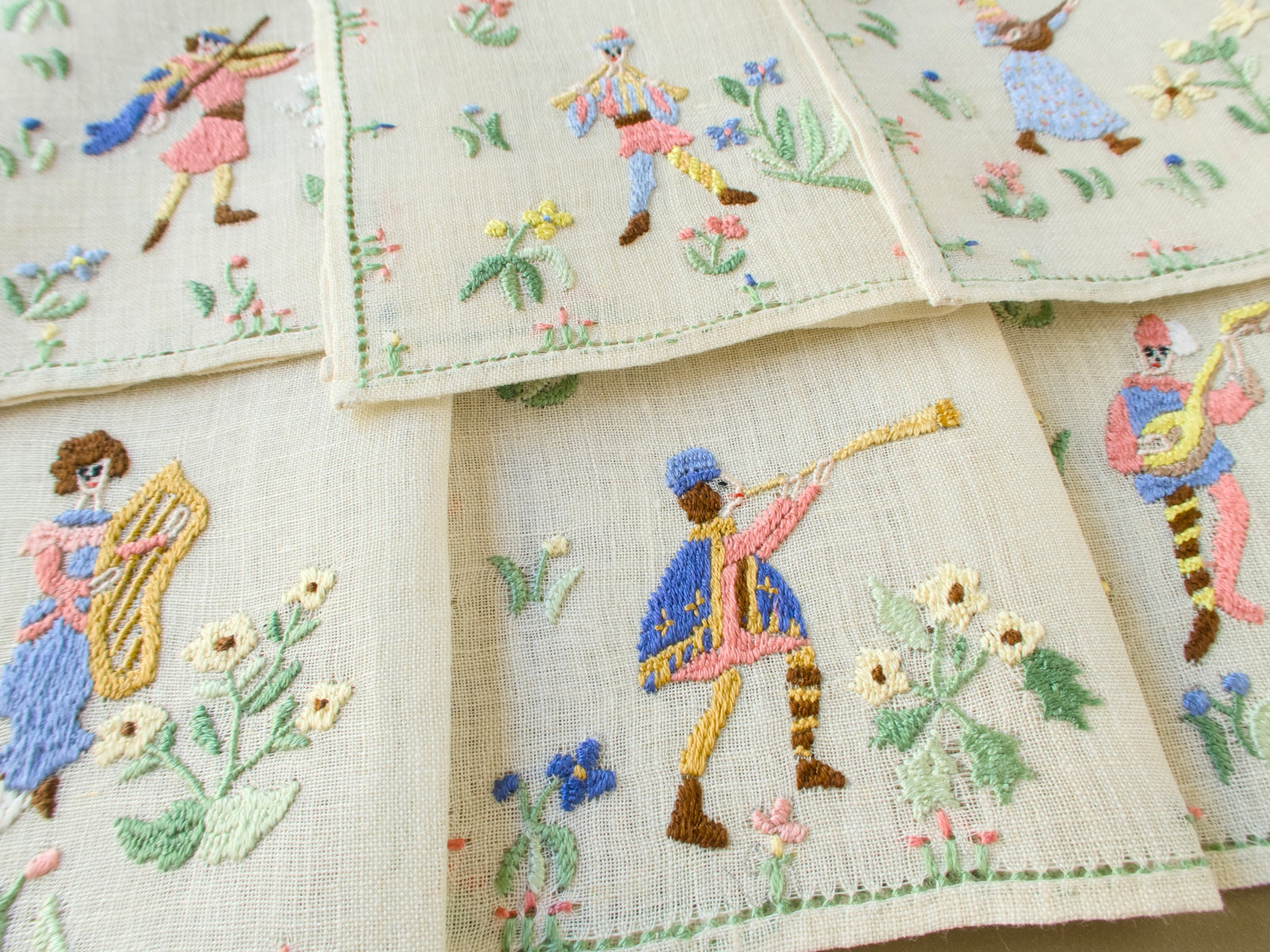 Vintage Baroness Rapisardi Medieval Musicians cocktail napkins hand embroidered in punto stuoia with a violinist, a piper, a harpist, a horn player and a lute player in colorful medieval dress, edged with a dainty floral border