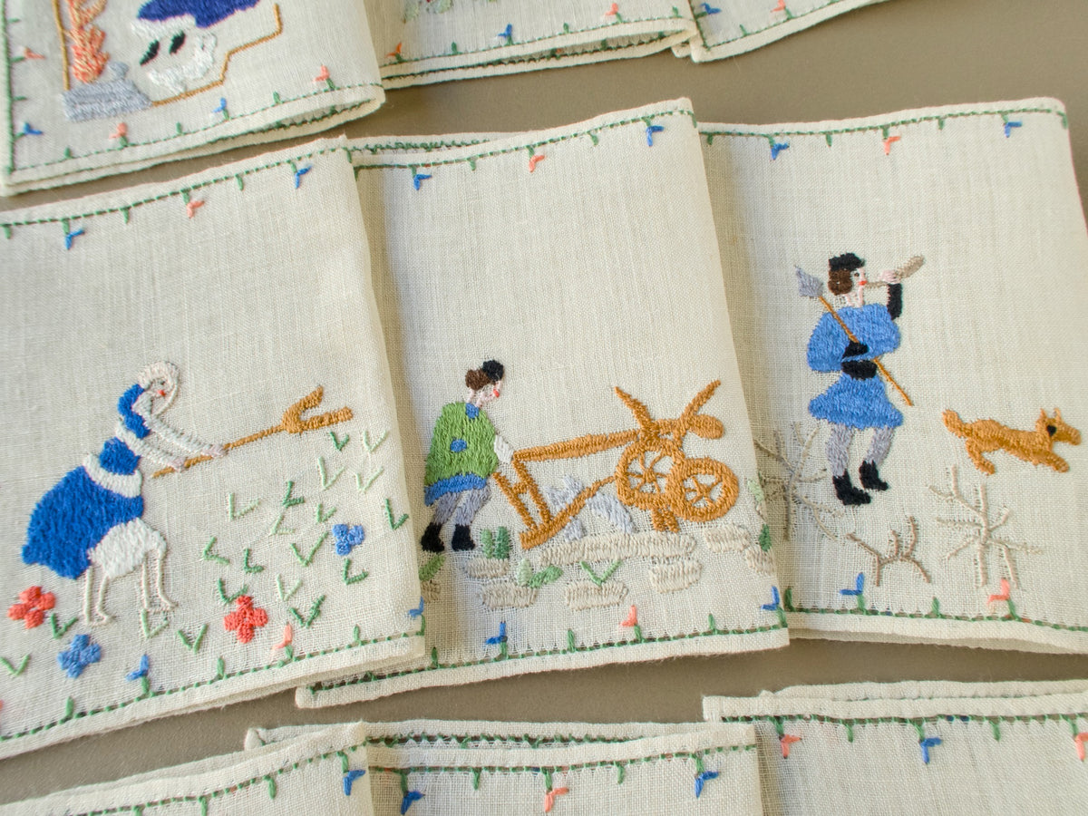 Three Baroness Rapisardi cocktail napkins showing a haymaker with a pitchfork, a farmer guiding a wooden plow and a hunter in blue with a spear and horn beside a small tan dog