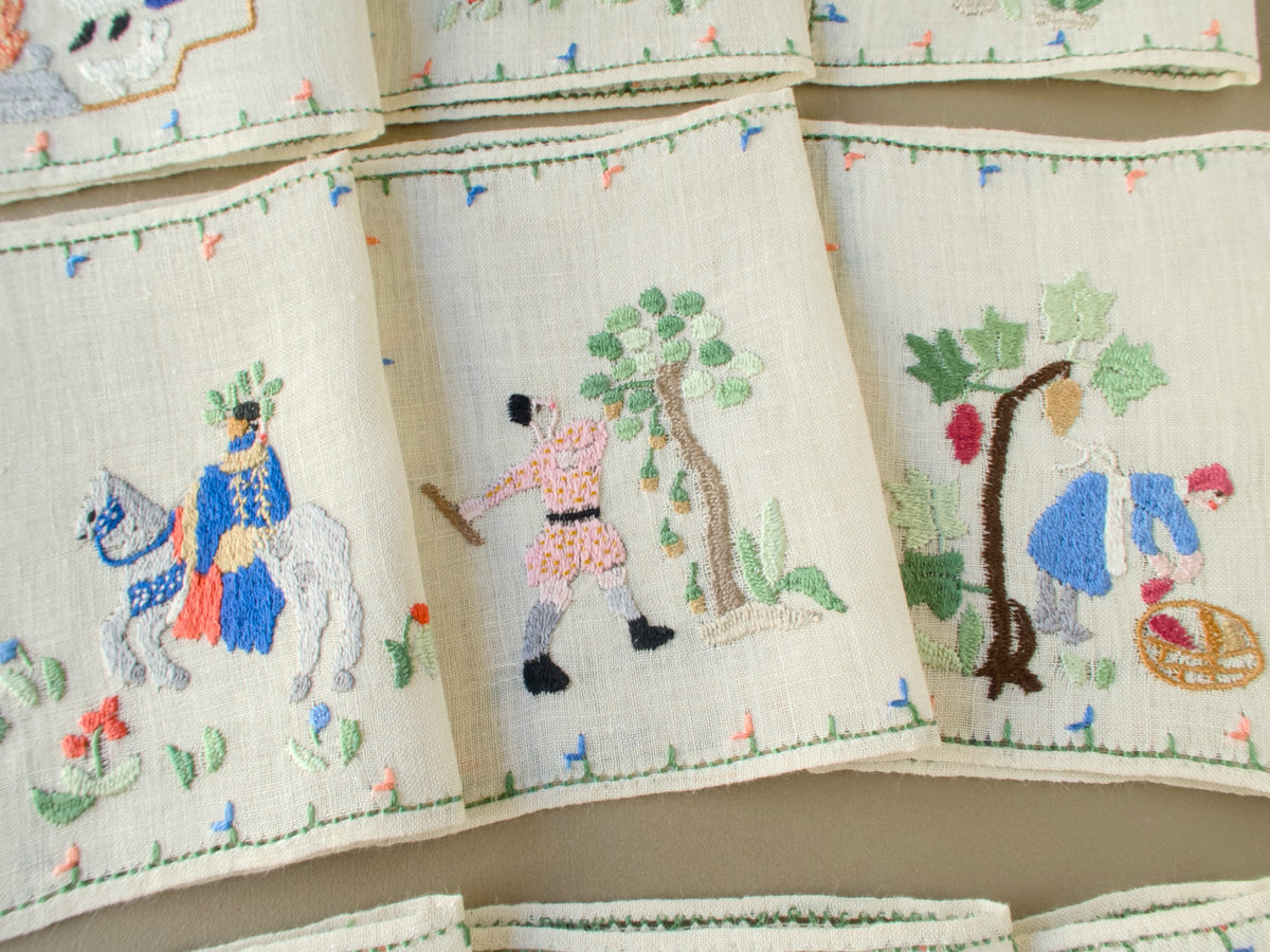 Three Baroness Rapisardi cocktail napkins showing a rider on a gray horse, a man in a pink tunic knocking acorns from an oak with a pole and a grape picker filling a basket under a vine