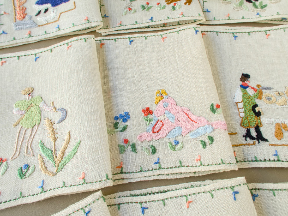 Three Baroness Rapisardi cocktail napkins showing a reaper with a sickle beside tall wheat, a figure in a pink gown reclining with a red flower and a man at a table set with round loaves