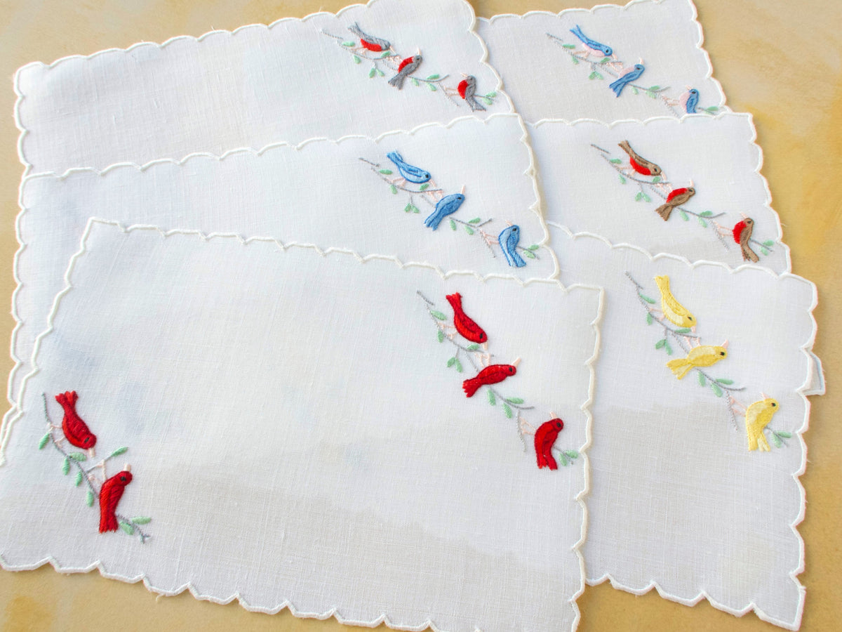 Vintage Madeira linen cocktail napkins embroidered with colorful songbirds, displayed in a layered arrangement.