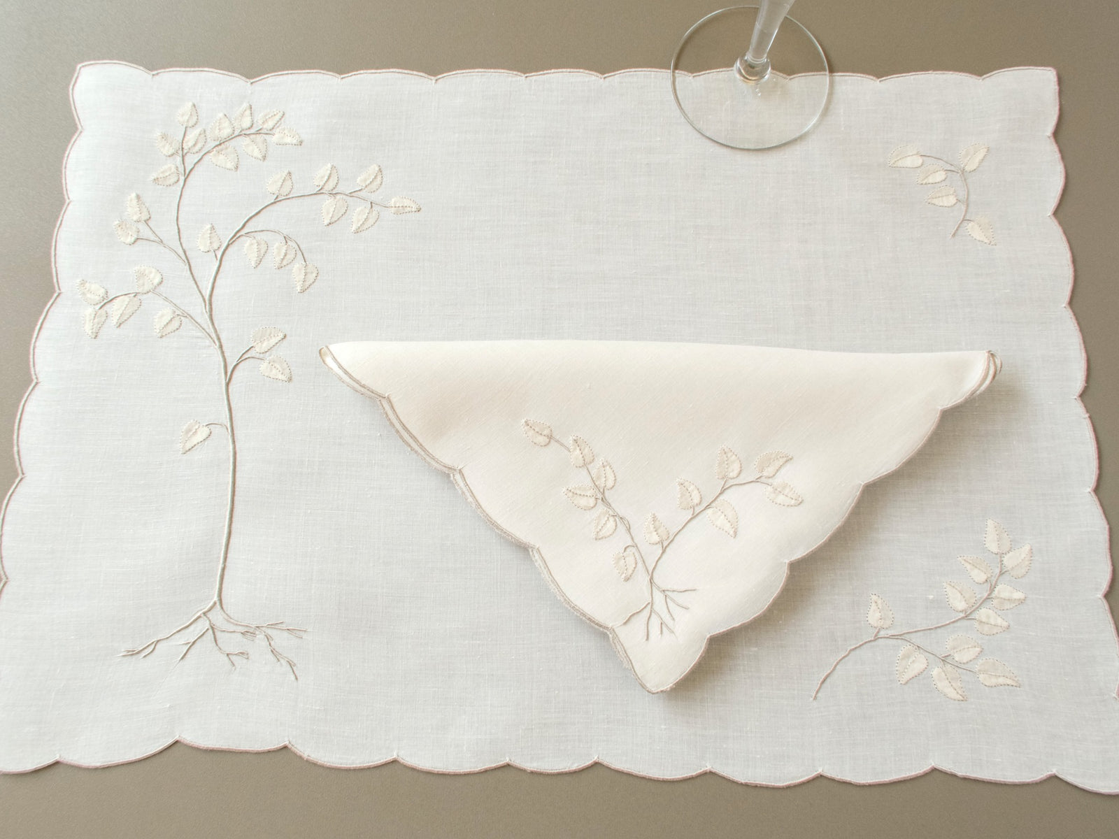 Vintage Madeira linen placemat with an appliquéd tree and roots, corner sprigs and a folded napkin with a leafy branch