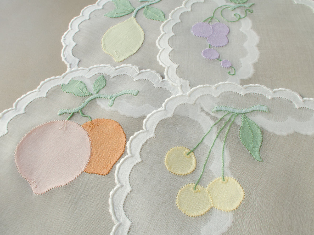 Set of eight vintage Madeira organdy cocktail rounds hand embroidered with fruit motifs in soft peach, green and lavender, with linen appliqué and scalloped caseado bastido edging