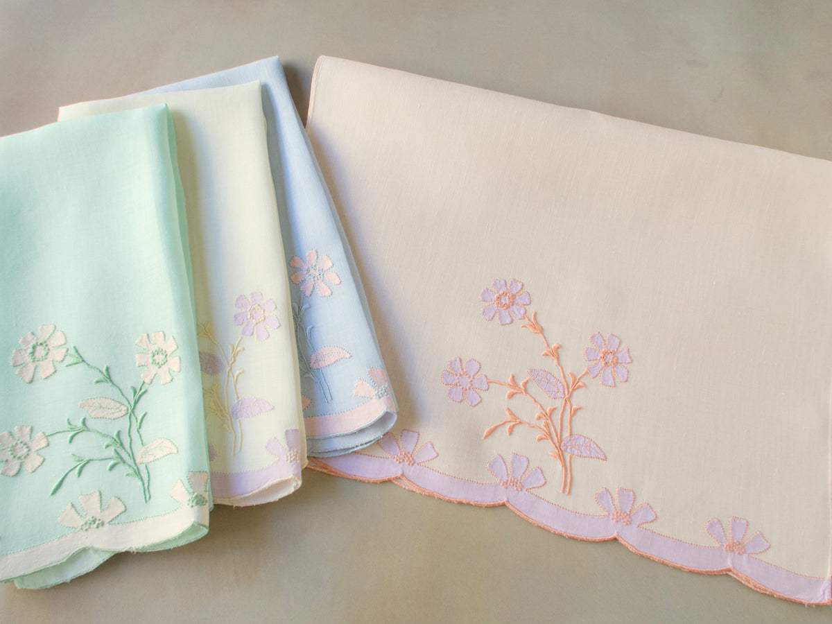 Vintage Madeira guest towels folded and stacked, showing delicate pastel floral embroidery on fine Irish linen in green and blue