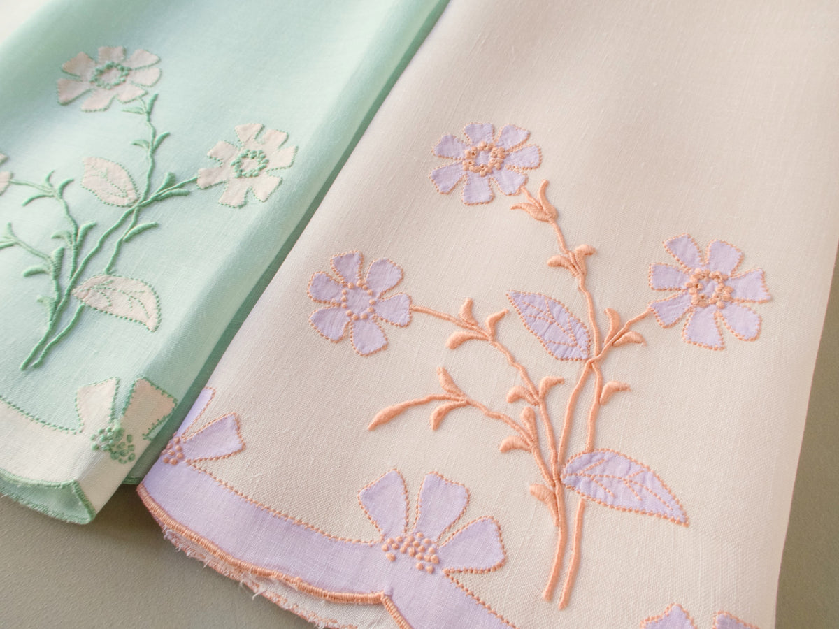 Detail of vintage Madeira guest towel hand embroidered with a delicate floral spray in peach and soft pink on fine Irish linen​​​​​​​​​​​​​​​​