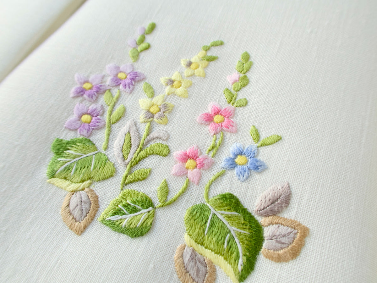 Closeup of a vintage Belgian linen guest towel hand embroidered in Madeira with colorful floral bouquet and scalloped edge.