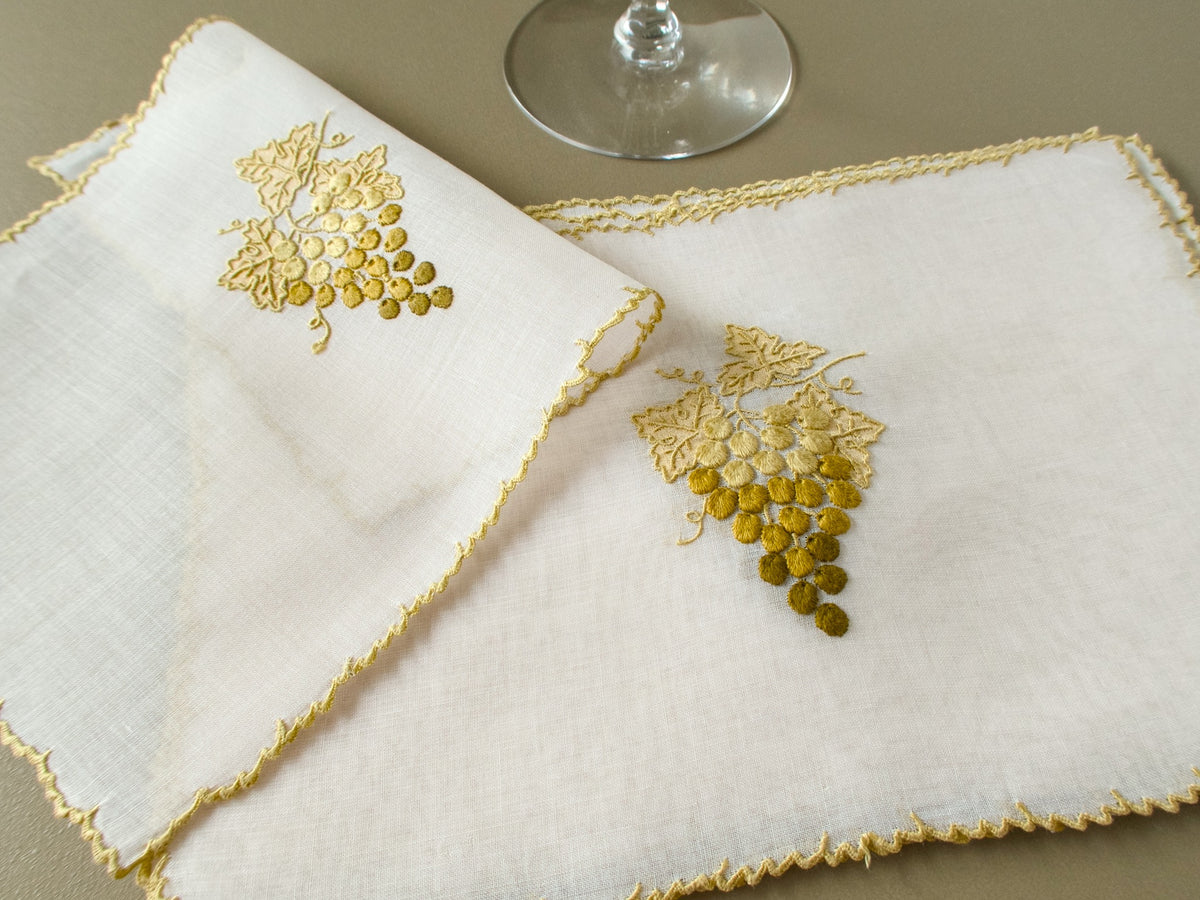 Vintage Marghab "Grape & Leaf" organdy cocktail napkins with embroidered gold and olive grapes and gold edging, beside a wine glass