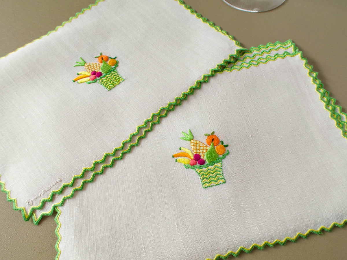 Vintage Marghab “Fruit Basket” cocktail napkins showing the embroidered fruit basket motif and green and yellow double-stitched hem treatment.