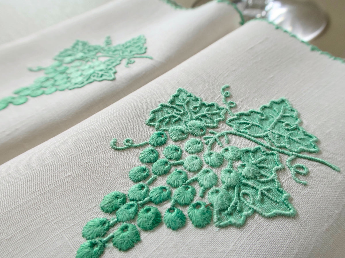 Close view of a vintage Marghab "Grape &amp; Leaf" napkin showing padded green grapes shading from light to deep, appliquéd vine leaves and curling tendrils on linen