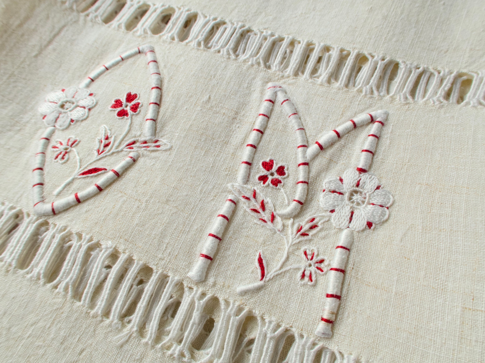 Full view of vintage French linen towel showing complete “OM” monogram embroidery in white and red with floral accents and knotted fringe edge