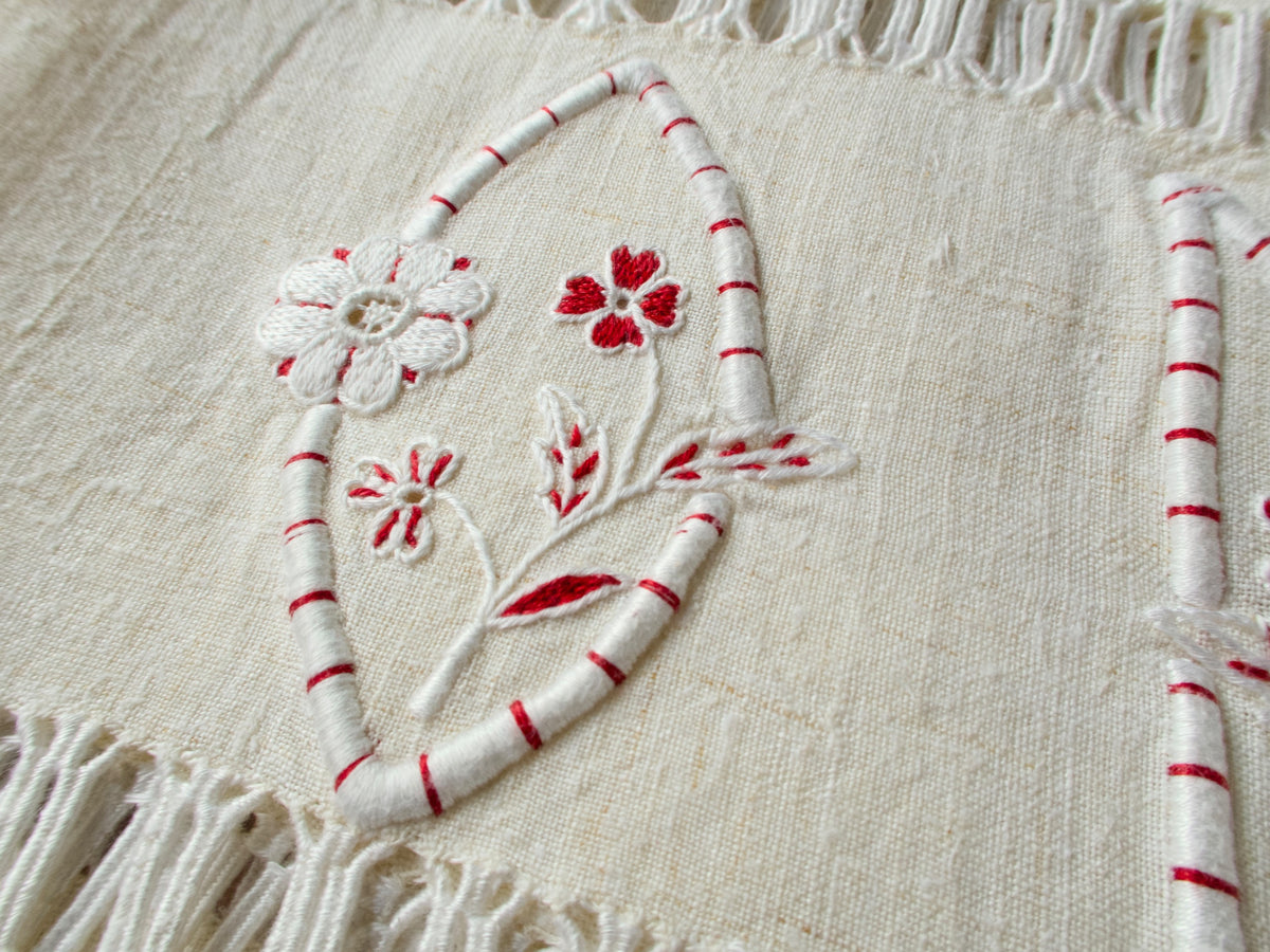 Detail of vintage French linen towel showing hand embroidered floral accent and red detailing alongside knotted fringe edge​​​​​​​​​​​​​​​​