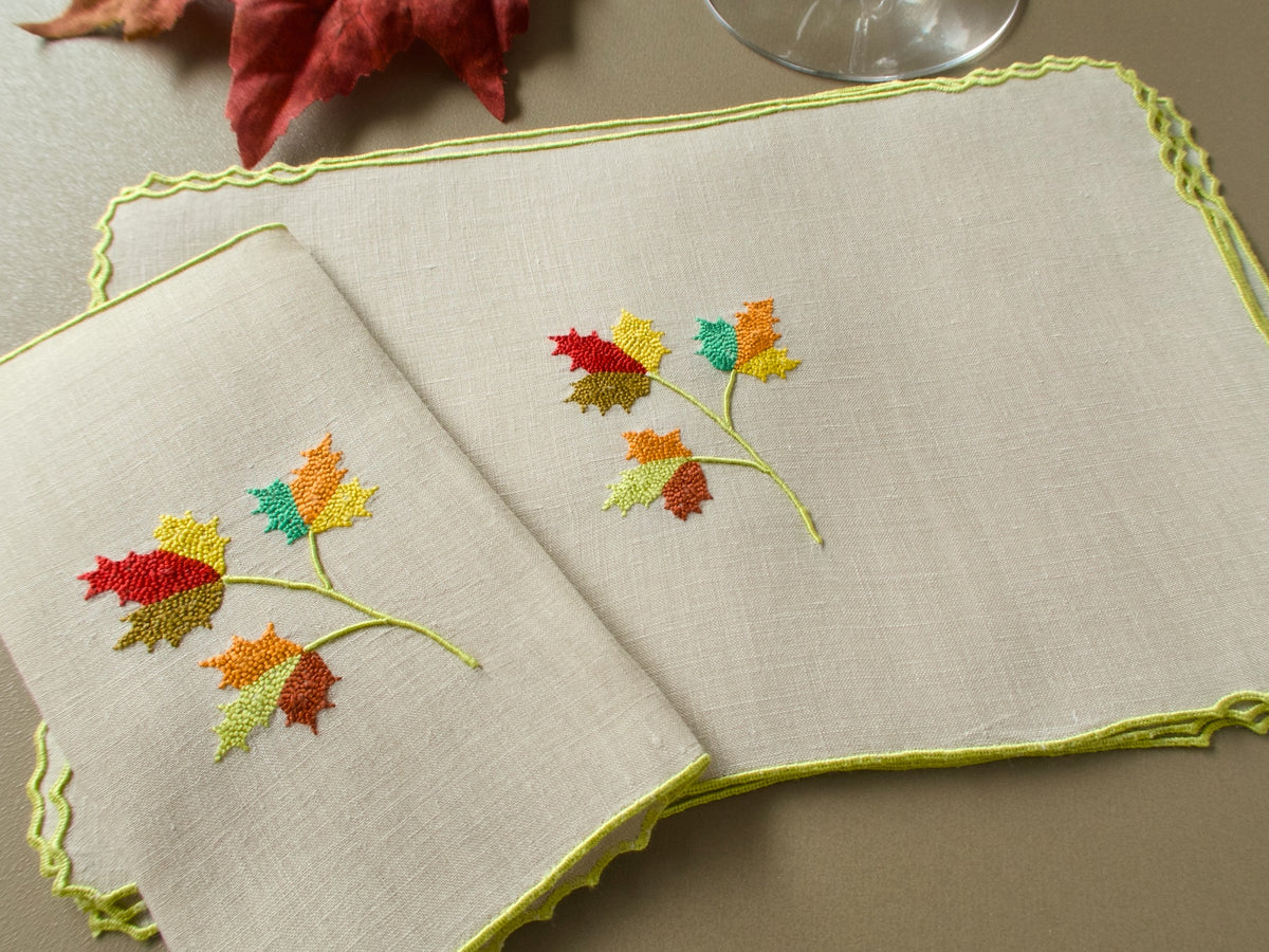 Two vintage Marghab “Maple Leaf” cocktail napkins showing colorful fall leaf embroidery and finely stitched edging on pale linen.