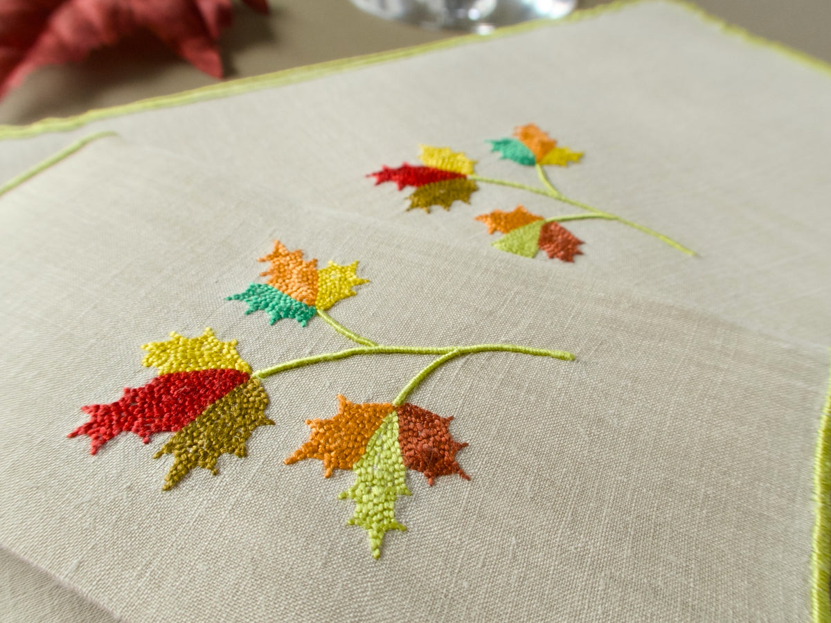 Detailed view of Marghab “Maple Leaf” cocktail napkins with richly colored hand embroidered leaves and fine linen texture.