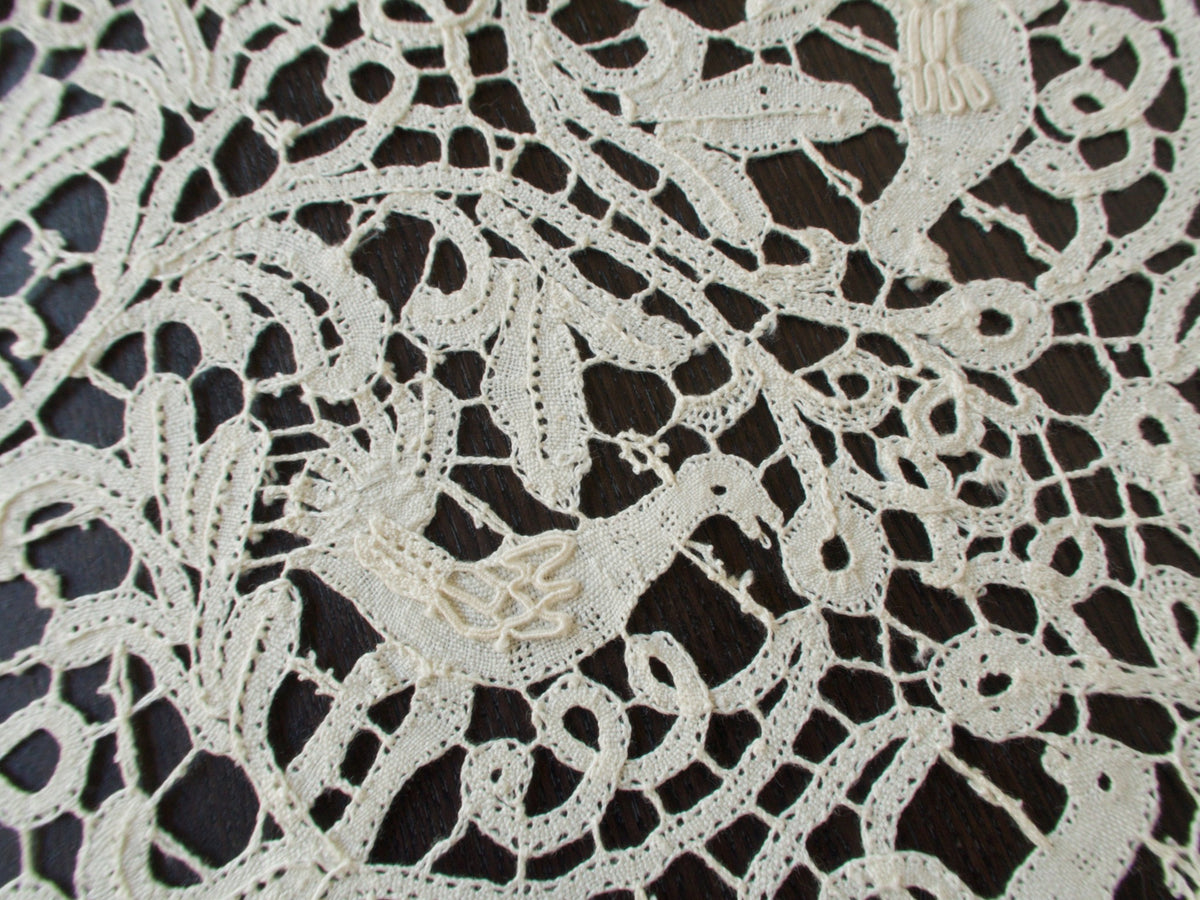 Close-up of intricate Italian bobbin lace pattern on a dark background