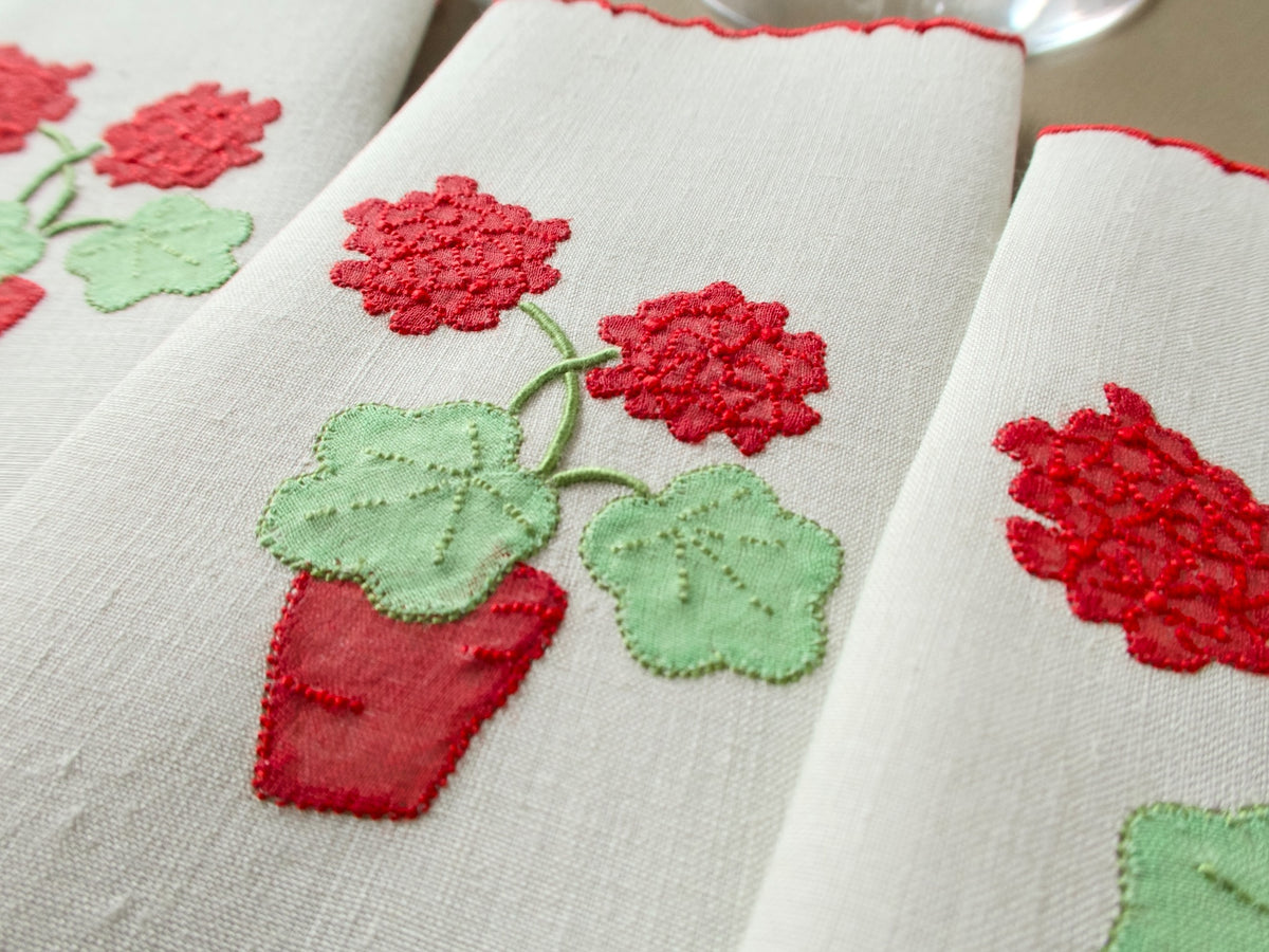 Close view of a vintage linen Marghab "Geranium" napkin showing two red geranium blossoms, green leaves and a red flowerpot appliquéd in organdy