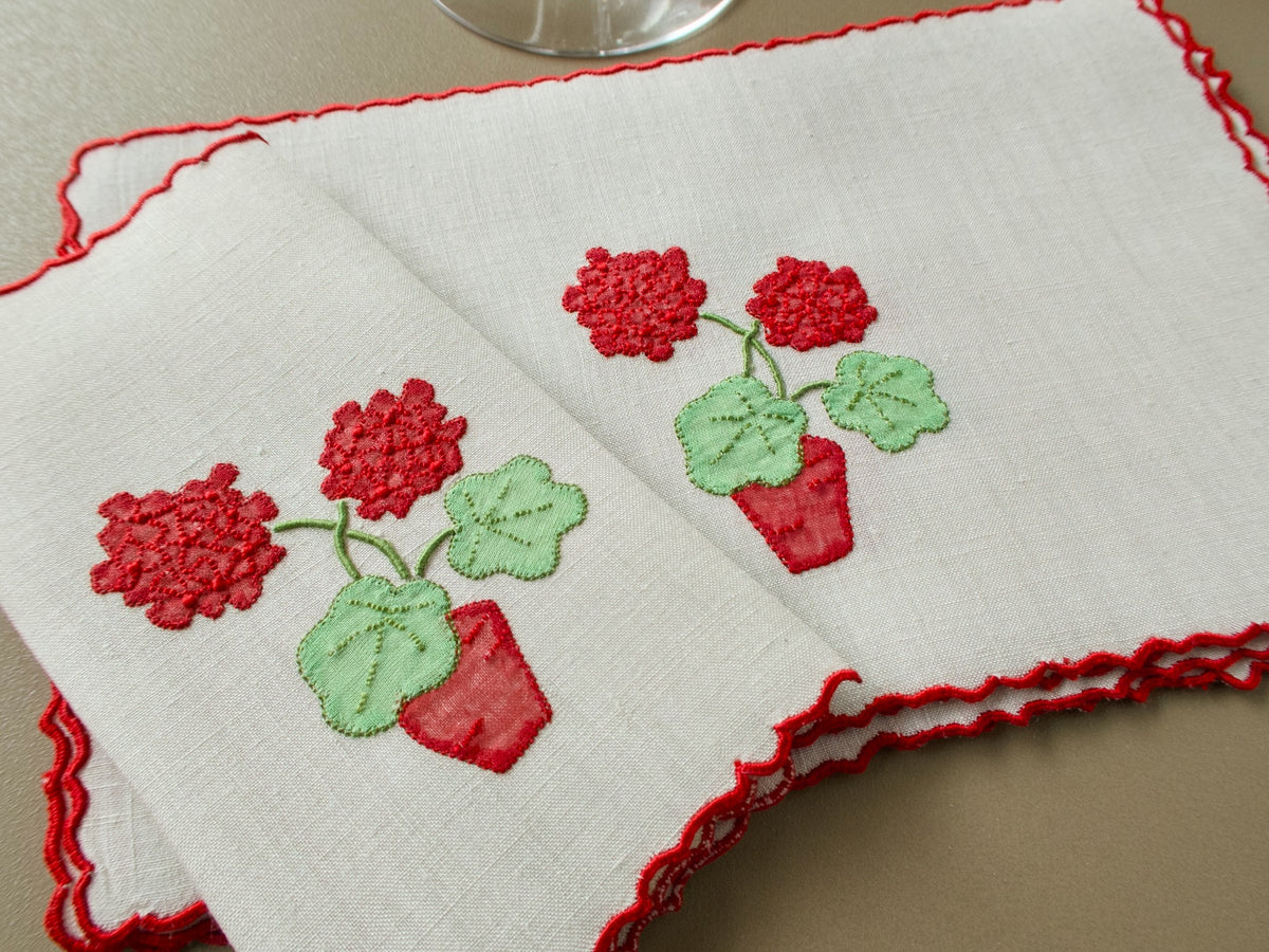 Vintage Marghab "Geranium" linen cocktail napkins with appliquéd red geranium blossoms, green leaves and a red flowerpot, edged in red scallops, beside a wine glass