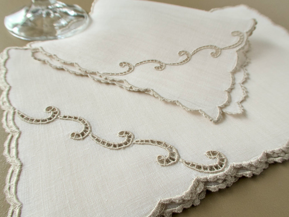 Stacked vintage Marghab "Simplicity" linen cocktail napkins, hand embroidered, with cutwork scrolls and scalloped edges, beside a wine glass