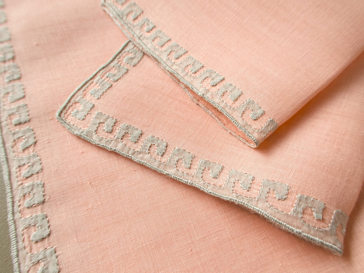 Close view of Marghab “Grecian Border” cocktail napkins showing the fine coral linen and detailed pale geometric embroidery.