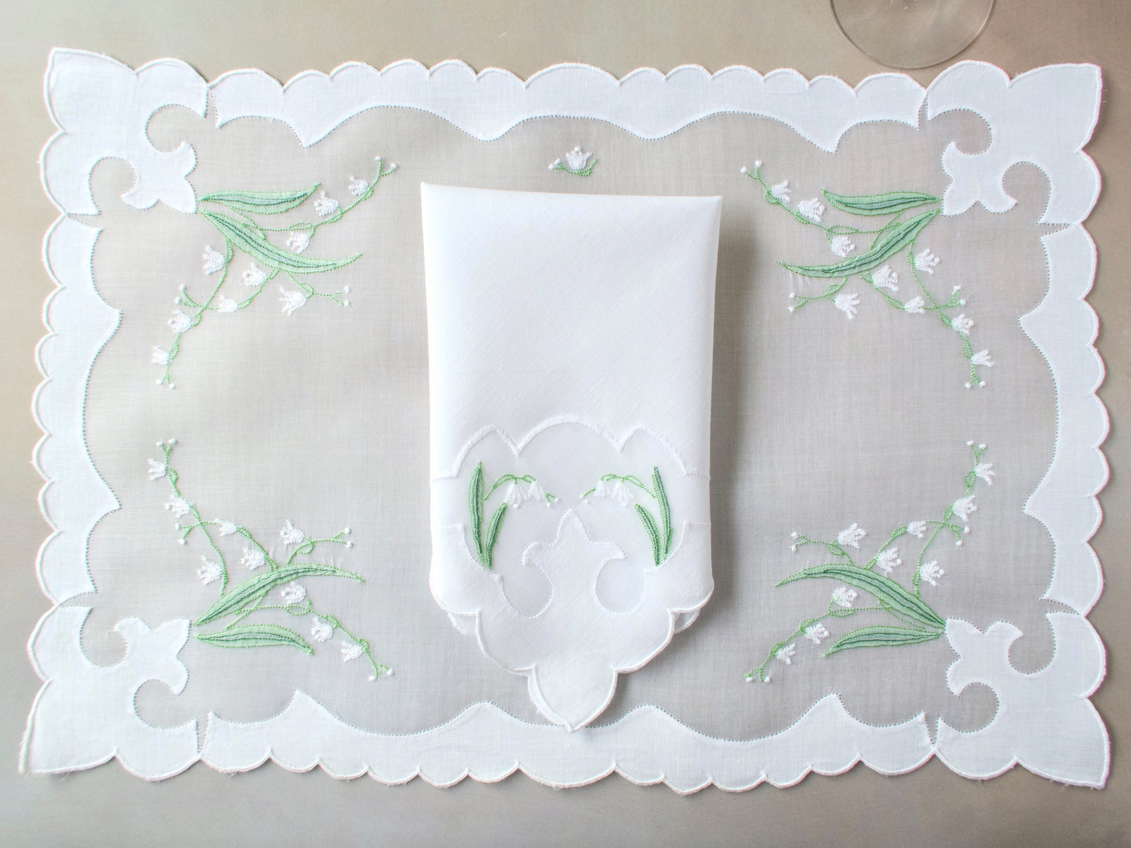 Full view of vintage Madeira lily of the valley organdy placemat with matching napkin centered on neutral beige surface.
