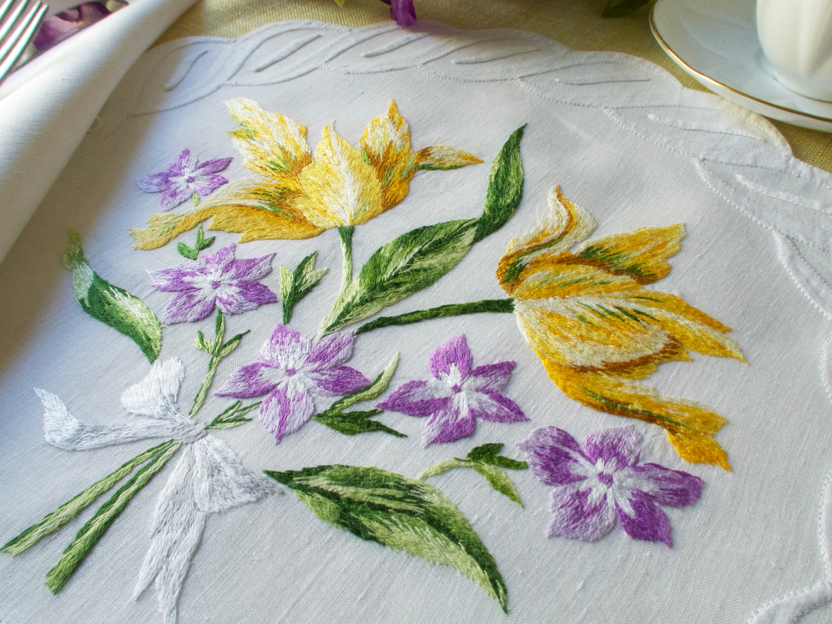 Hand-embroidered French linen placemat featuring yellow flowers with green leaves, part of a D. Porthault floral set.