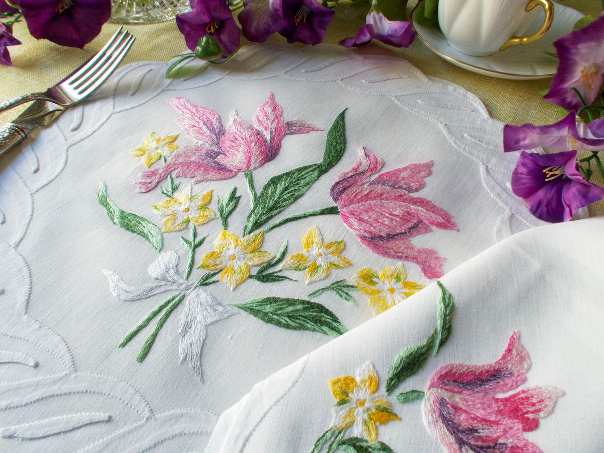 Close-up of vintage French linen placemat hand embroidered with pink and yellow flowers and scalloped edge.