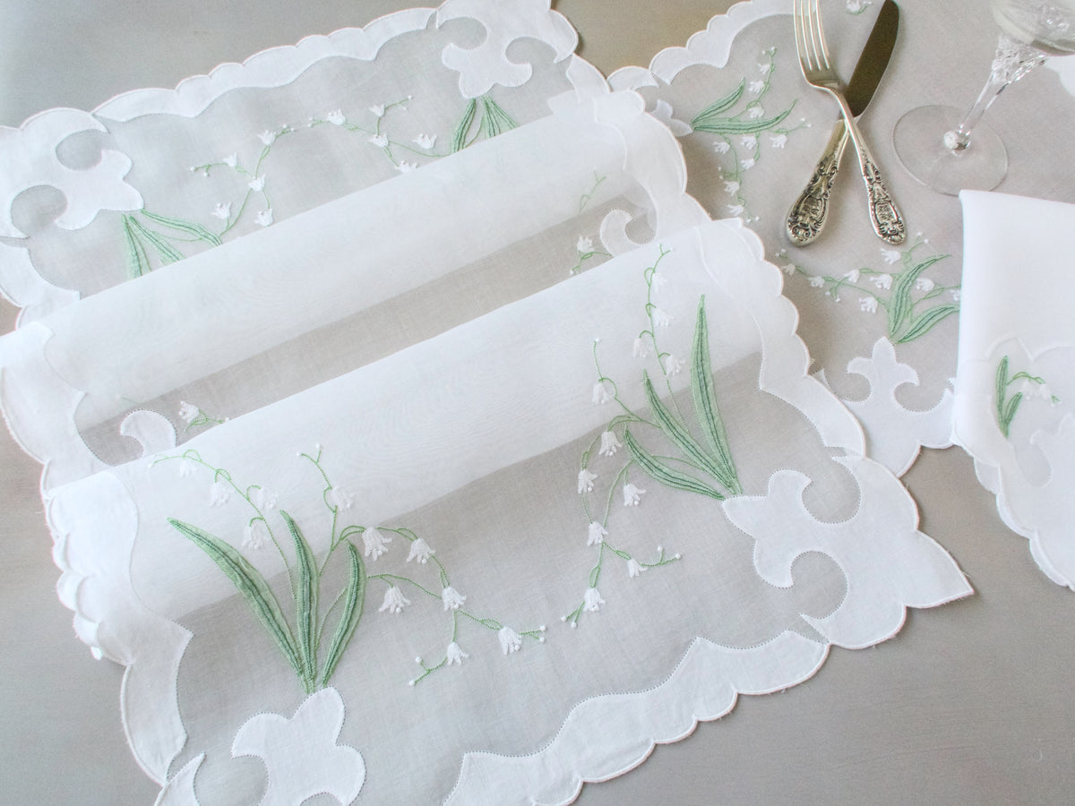 Gently folded vintage Madeira organdy table runner showing sheer fabric, scalloped cutwork edge, and hand embroidered lily of the valley motif.