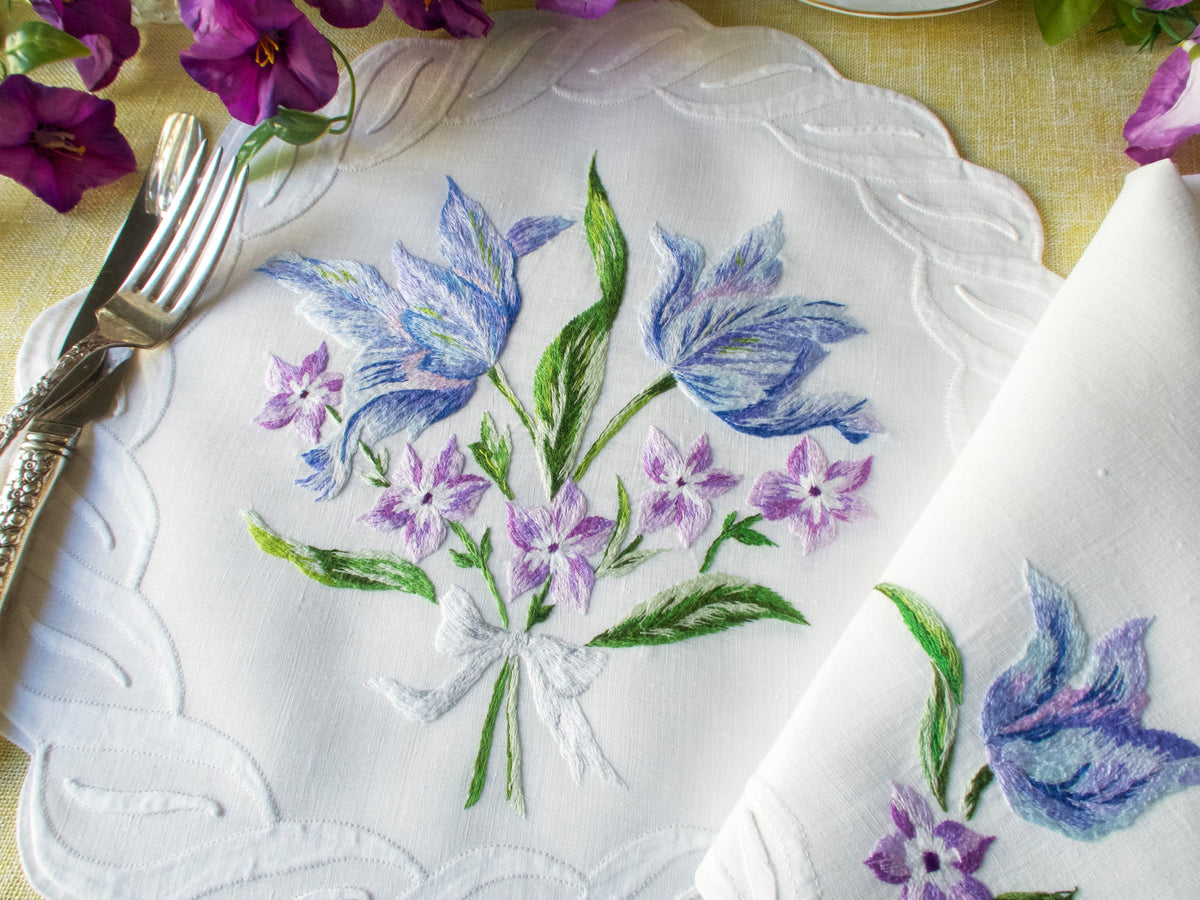 Blue and lavender floral embroidery on a vintage linen placemat with matching napkin folded beside.