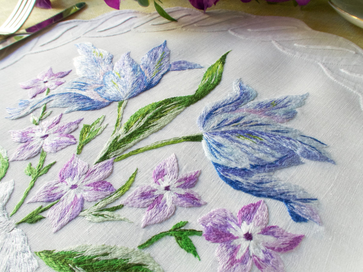 Vintage French linen placemat embroidered with delicate blue and white flowers, showing fine stitching.