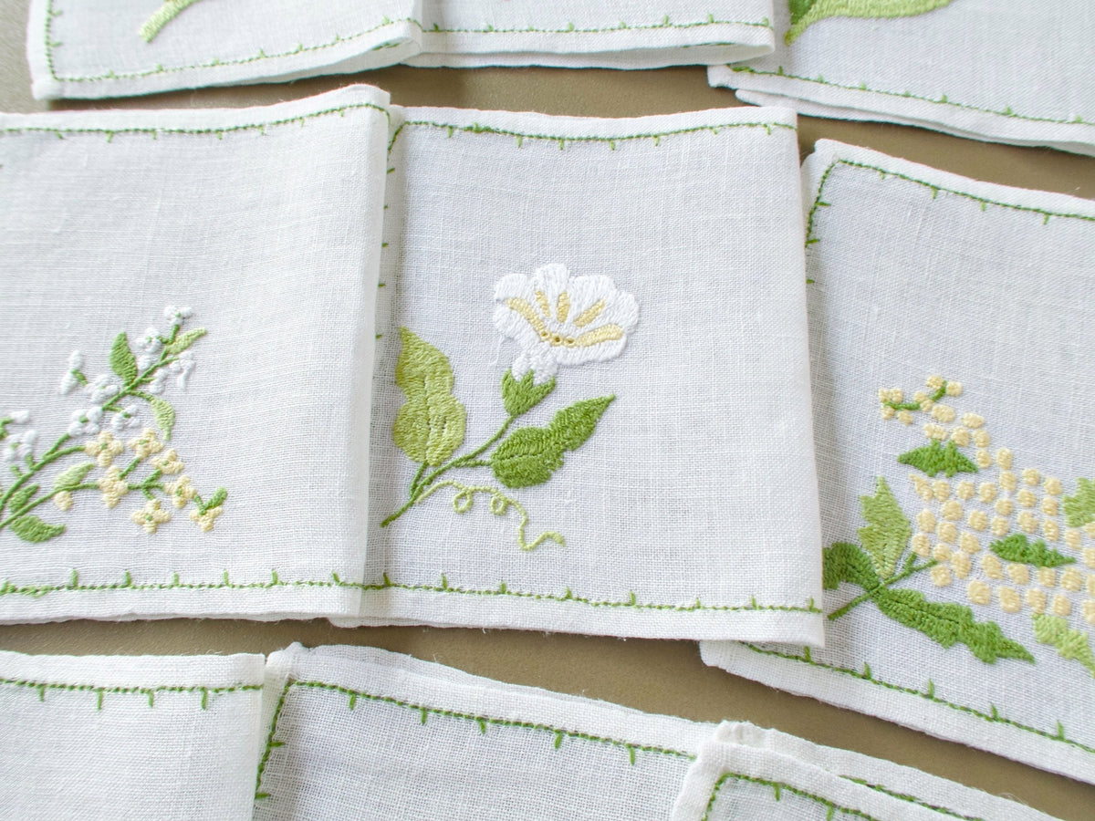 Three Baroness Rapisardi floral cocktail napkins with distinct botanical motifs and delicate green hand-stitched borders.