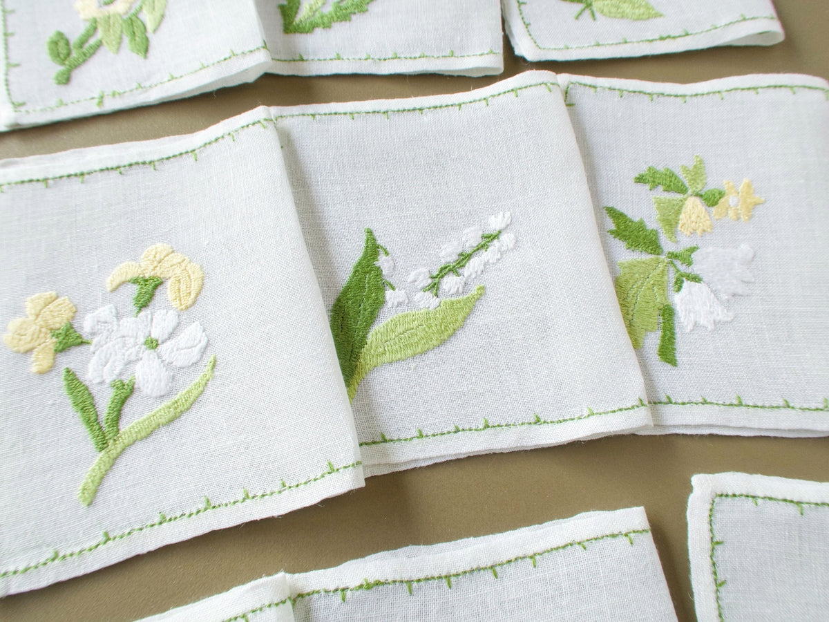 Three vintage Rapisardi cocktail napkins showing different hand embroidered floral designs in soft yellow, white and green.