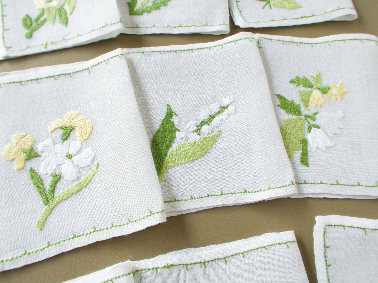 Three vintage Rapisardi cocktail napkins showing different hand embroidered floral designs in soft yellow, white and green.