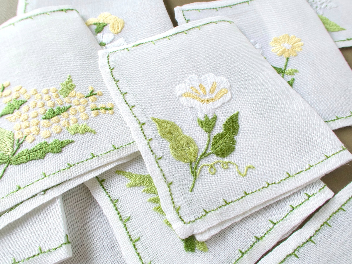 Close up of Baroness Rapisardi floral cocktail napkins highlighting dimensional embroidery and varied blossoms on semi sheer linen.