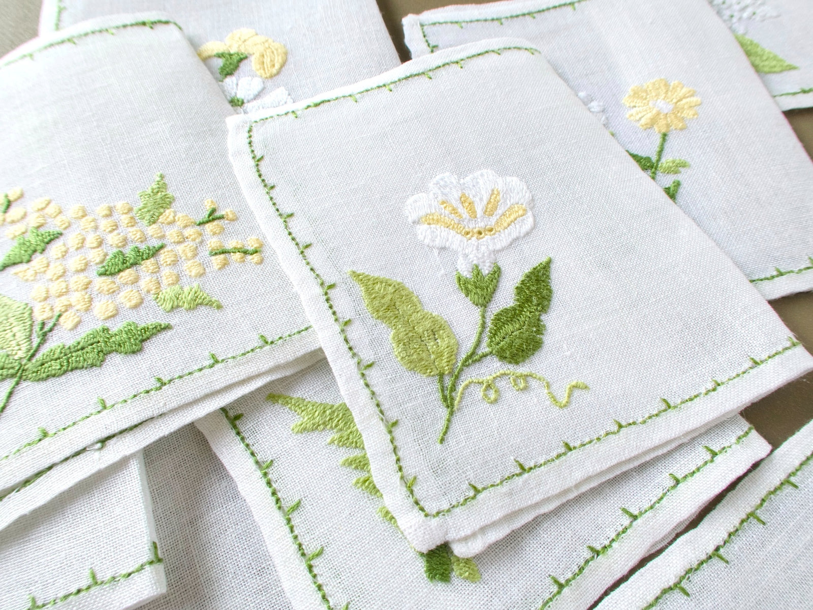 Close up of Baroness Rapisardi floral cocktail napkins highlighting dimensional embroidery and varied blossoms on semi sheer linen.