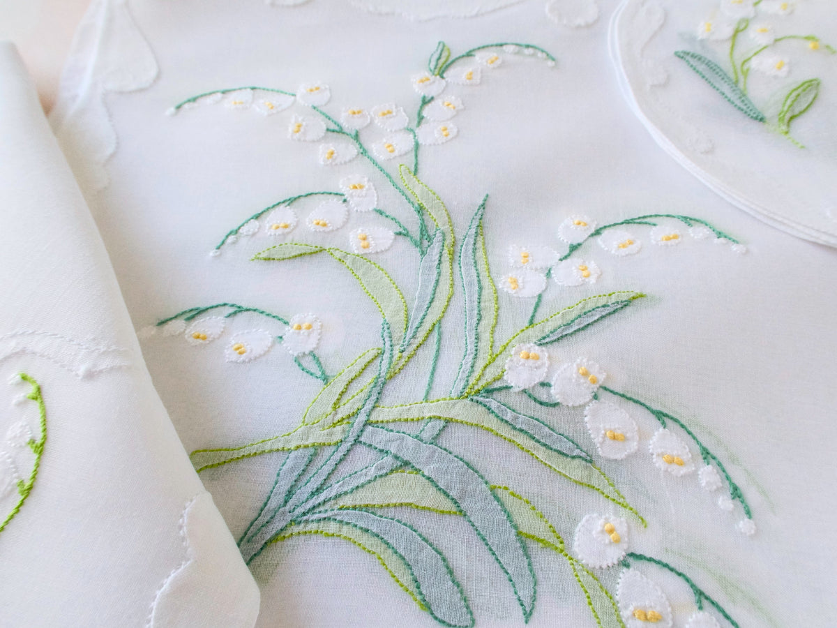 Close-up of hand embroidered Lily of the Valley on sheer organdy placemat, Madeira shadow work with white blossoms and yellow centers.