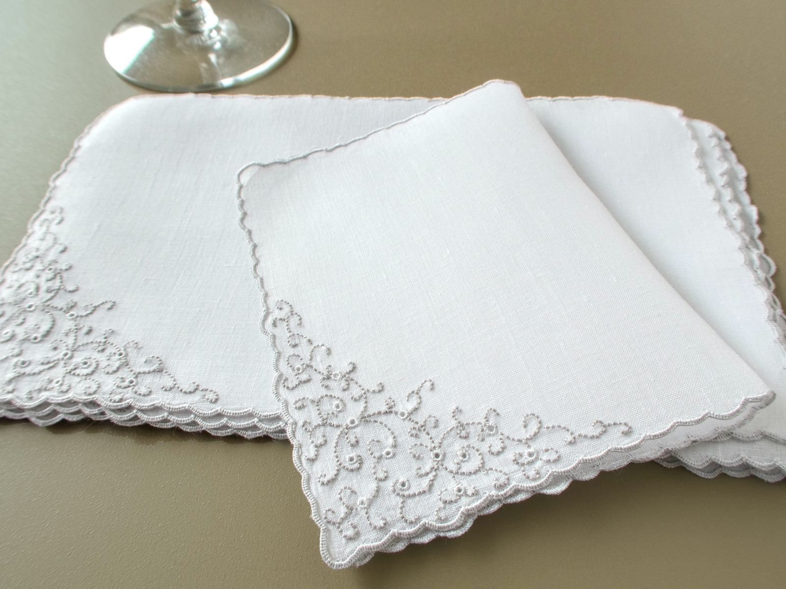 Stcked group of vintage Marghab “Thousand Eye” linen cocktail napkins with intricate hand embroidery and scalloped edges.