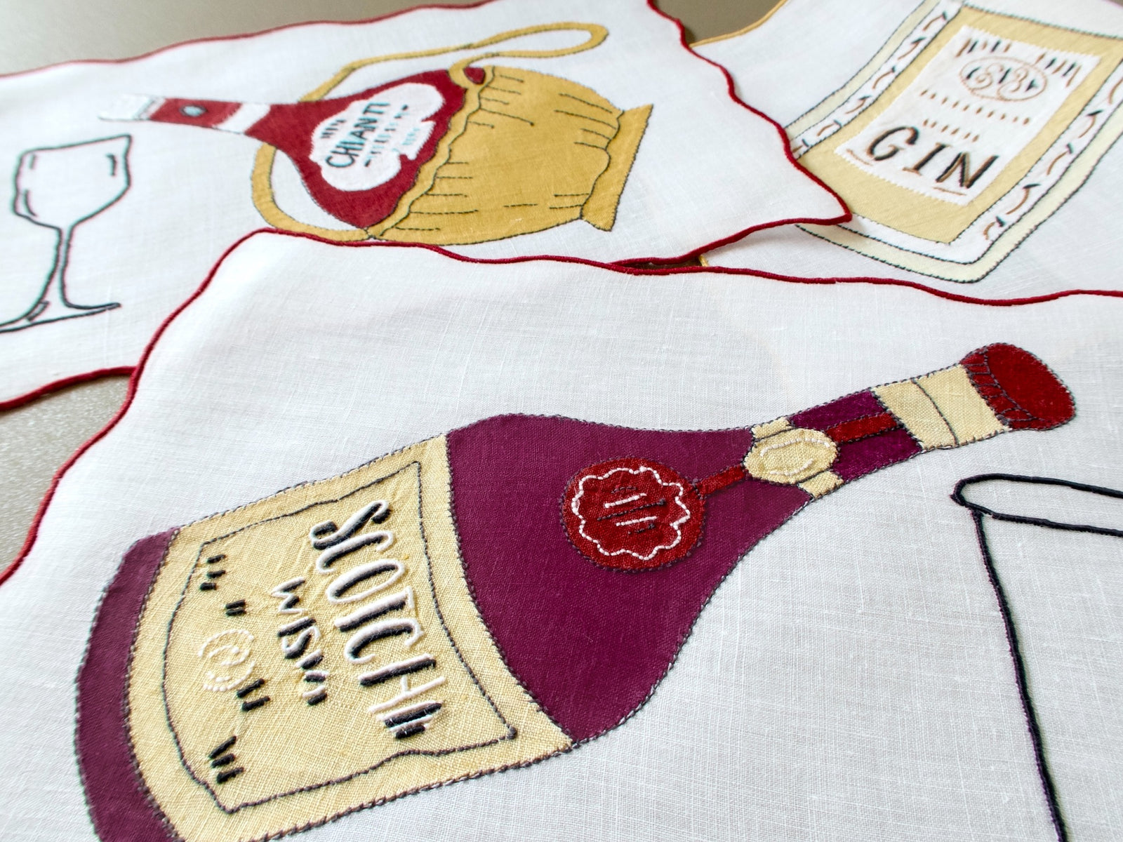 Close view of vintage Madeira cocktail napkins with appliqué wine and liquor bottles and embroidered glasses on linen