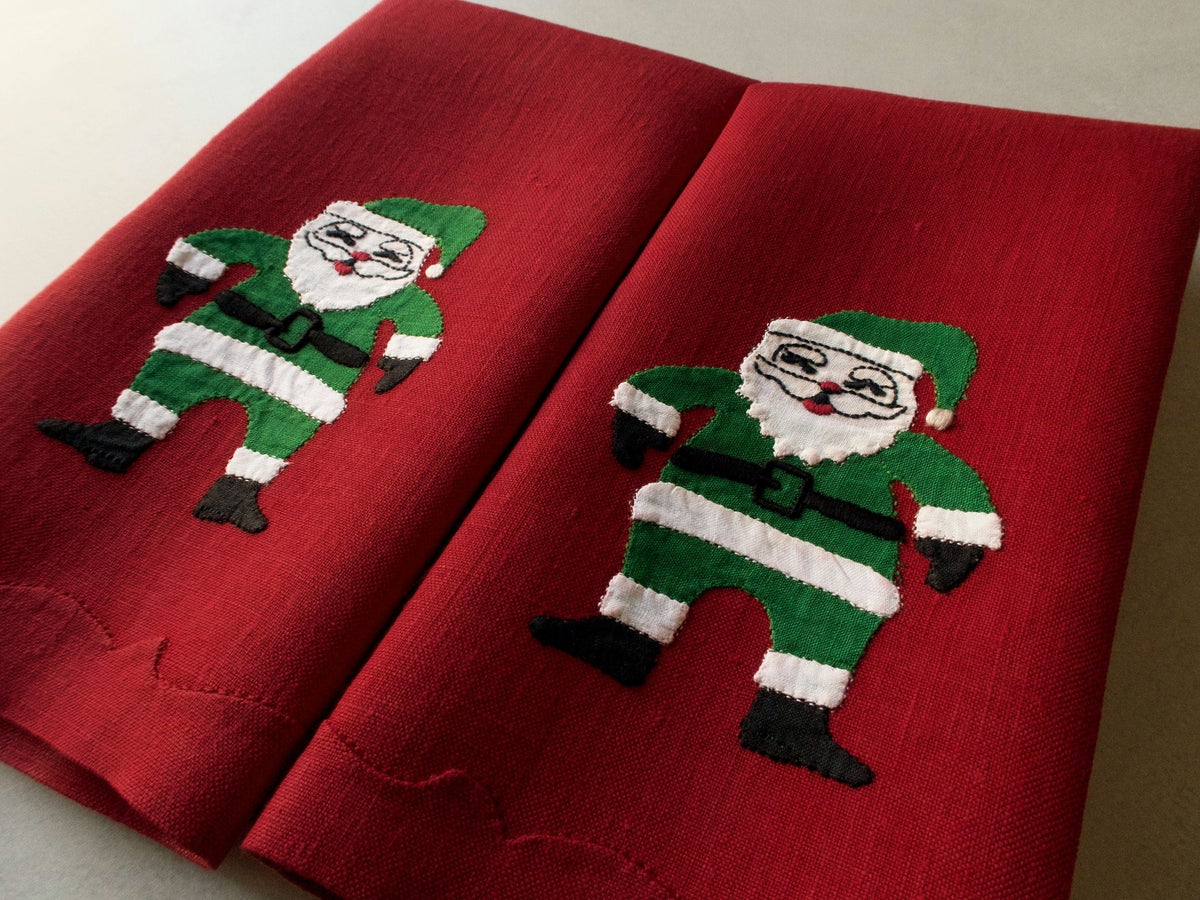 Red linen guest towels with green-and-white appliqué Santa figure, shown folded side by side.