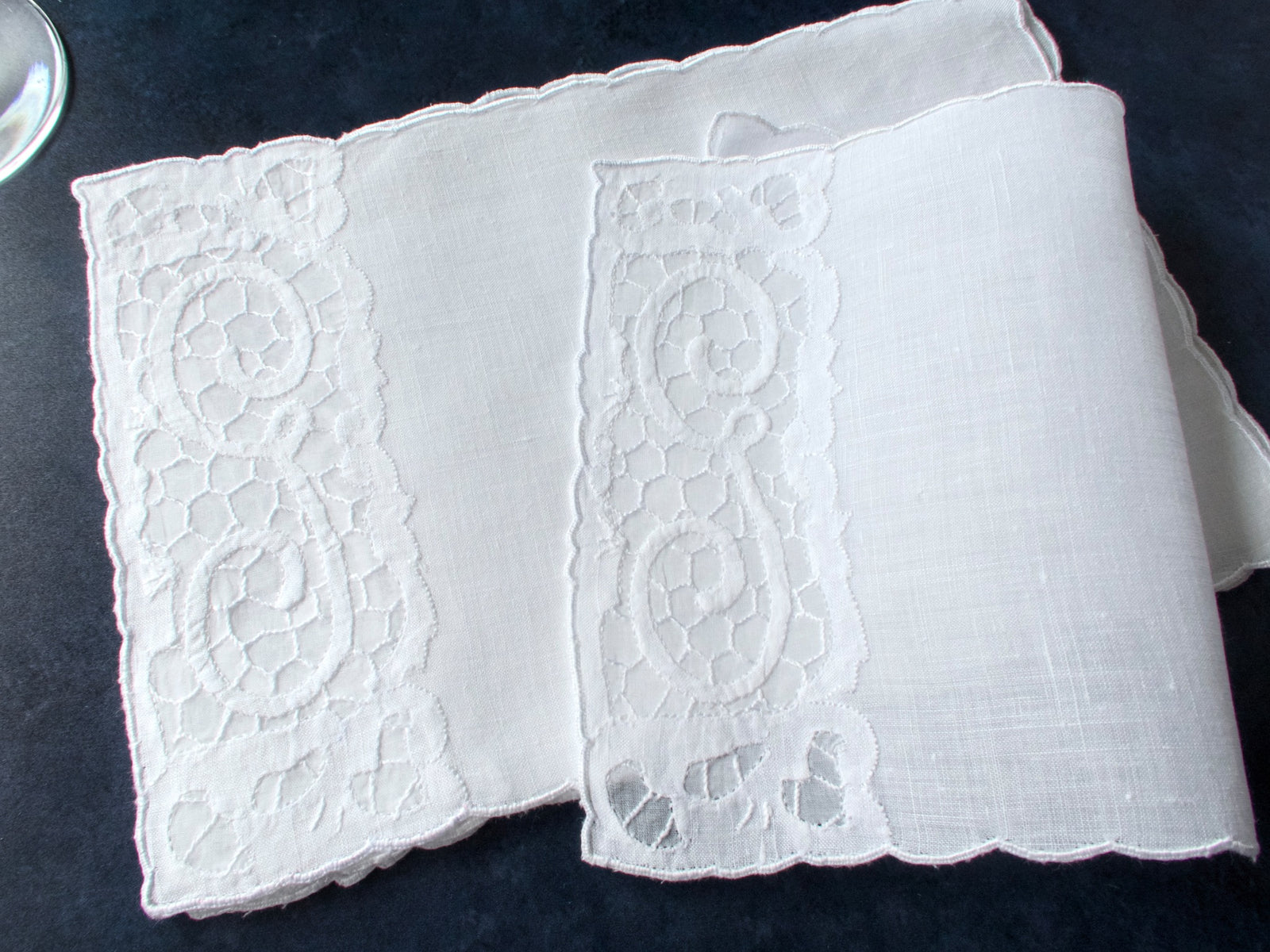 Folded vintage Madeira linen cocktail napkins with an embroidered G monogram, stacked on a dark background