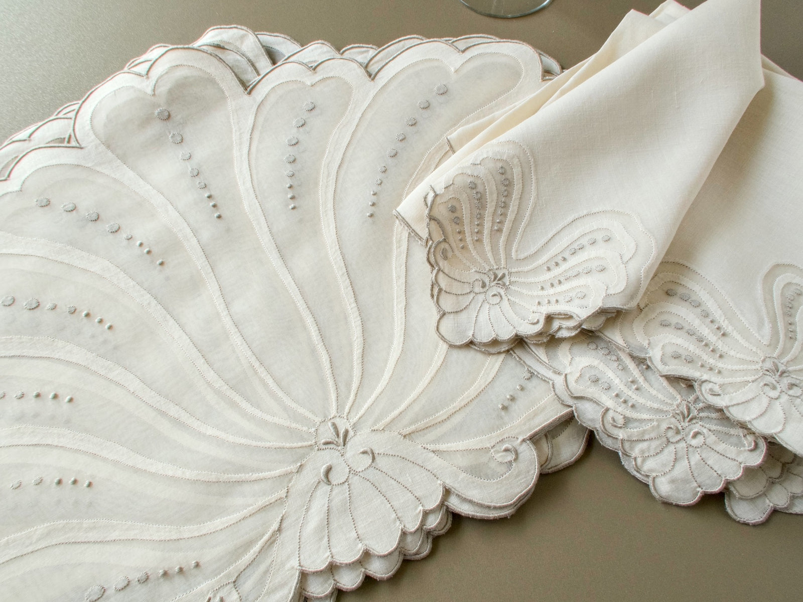 Stacked vintage Madeira fan-shaped placemats beside linen napkins with a matching fan corner