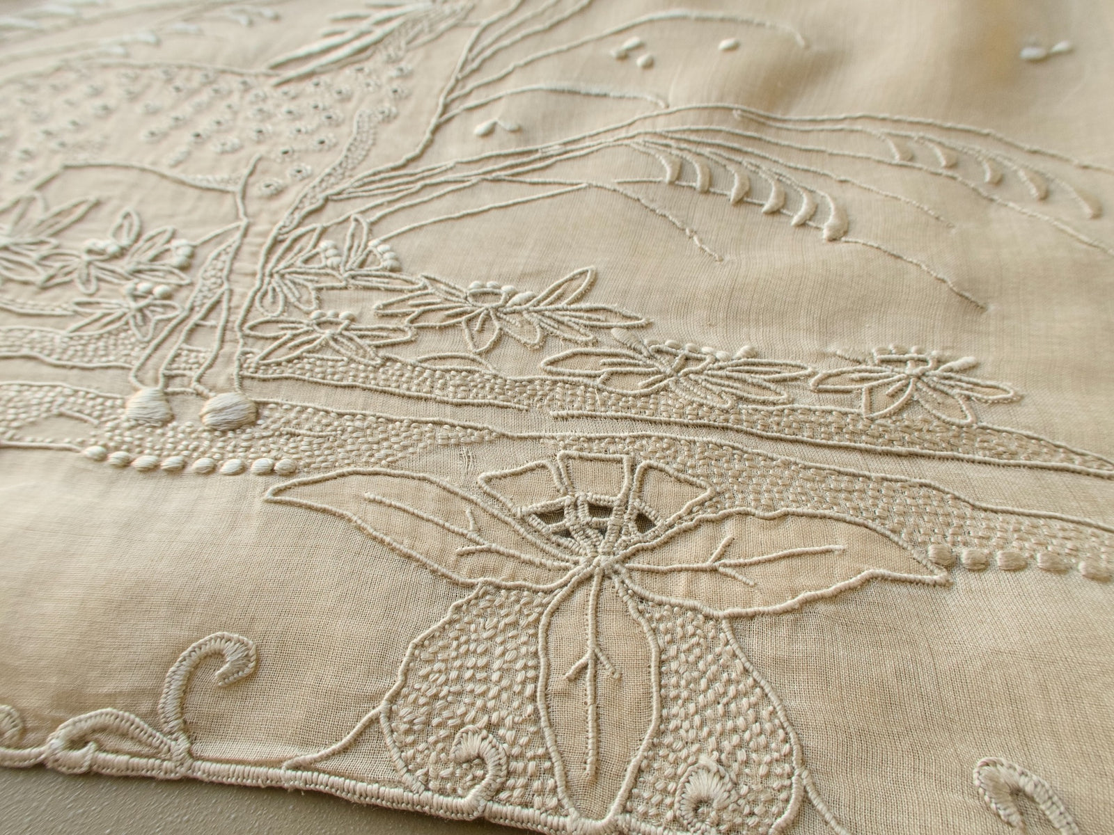 Angled view of the raised embroidery at the deer's hooves and flowers on a vintage Marghab organdy pillow cover