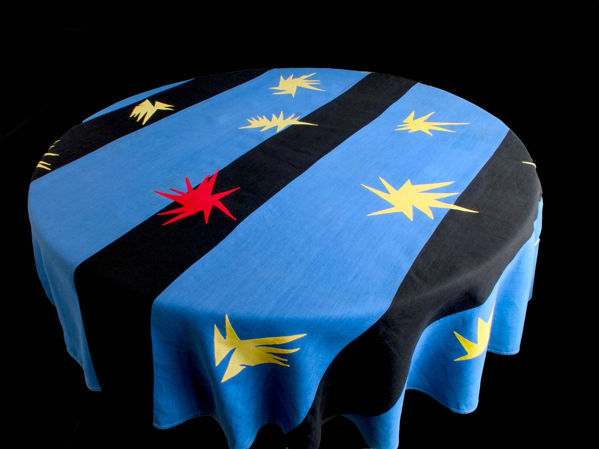 Vintage Porthault ‘Cirque’ tablecloth in blue, black, and red with starburst motifs inspired by Matisse, shown draped on a round table.