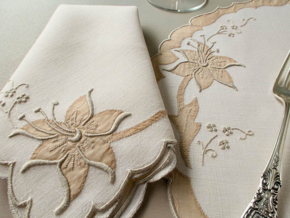 Close-up of vintage Madeira placemat and folded napkin showing richly dimensional lily in organdy appliqué on ecru linen with scalloped organdy appliqué border