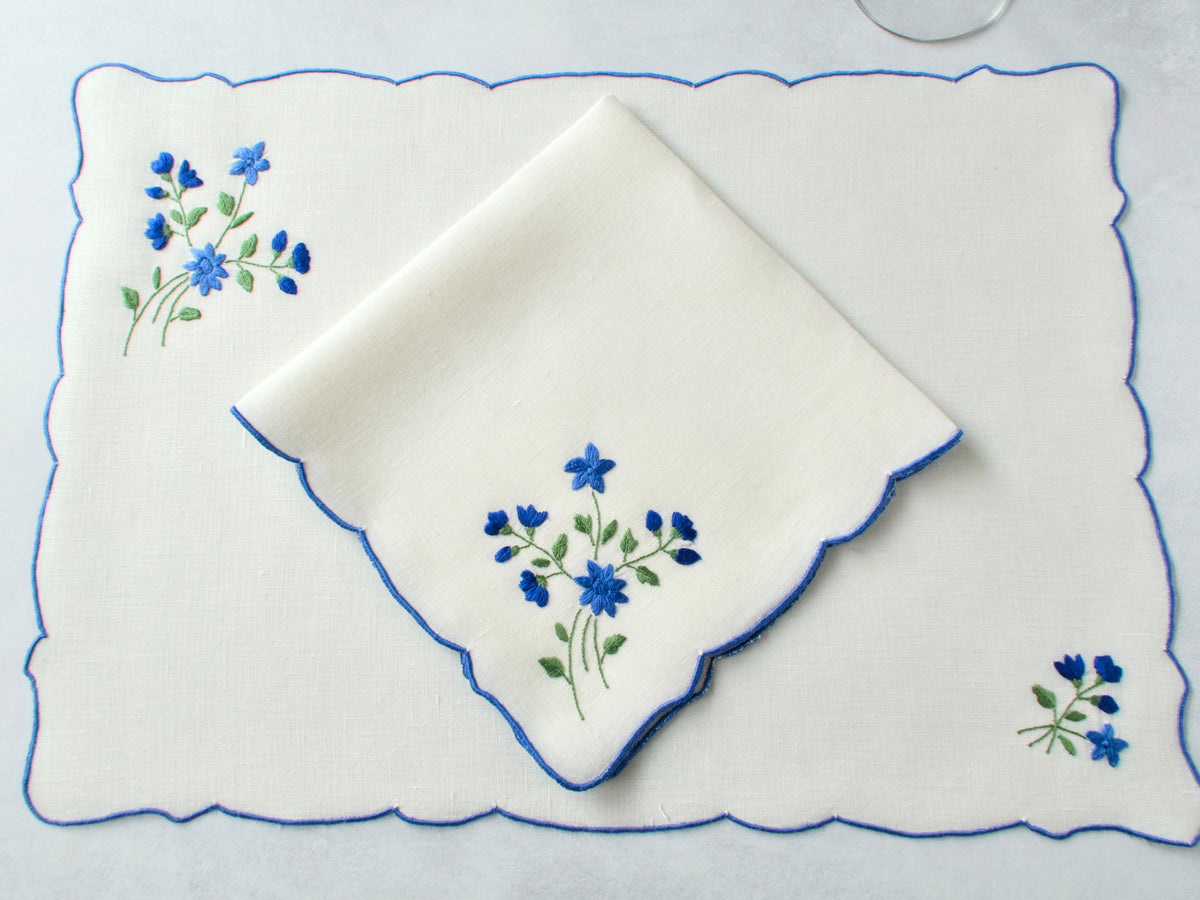 Folded vintage Madeira napkin and placemat showing blue forget-me-not embroidery and blue scalloped edge detail