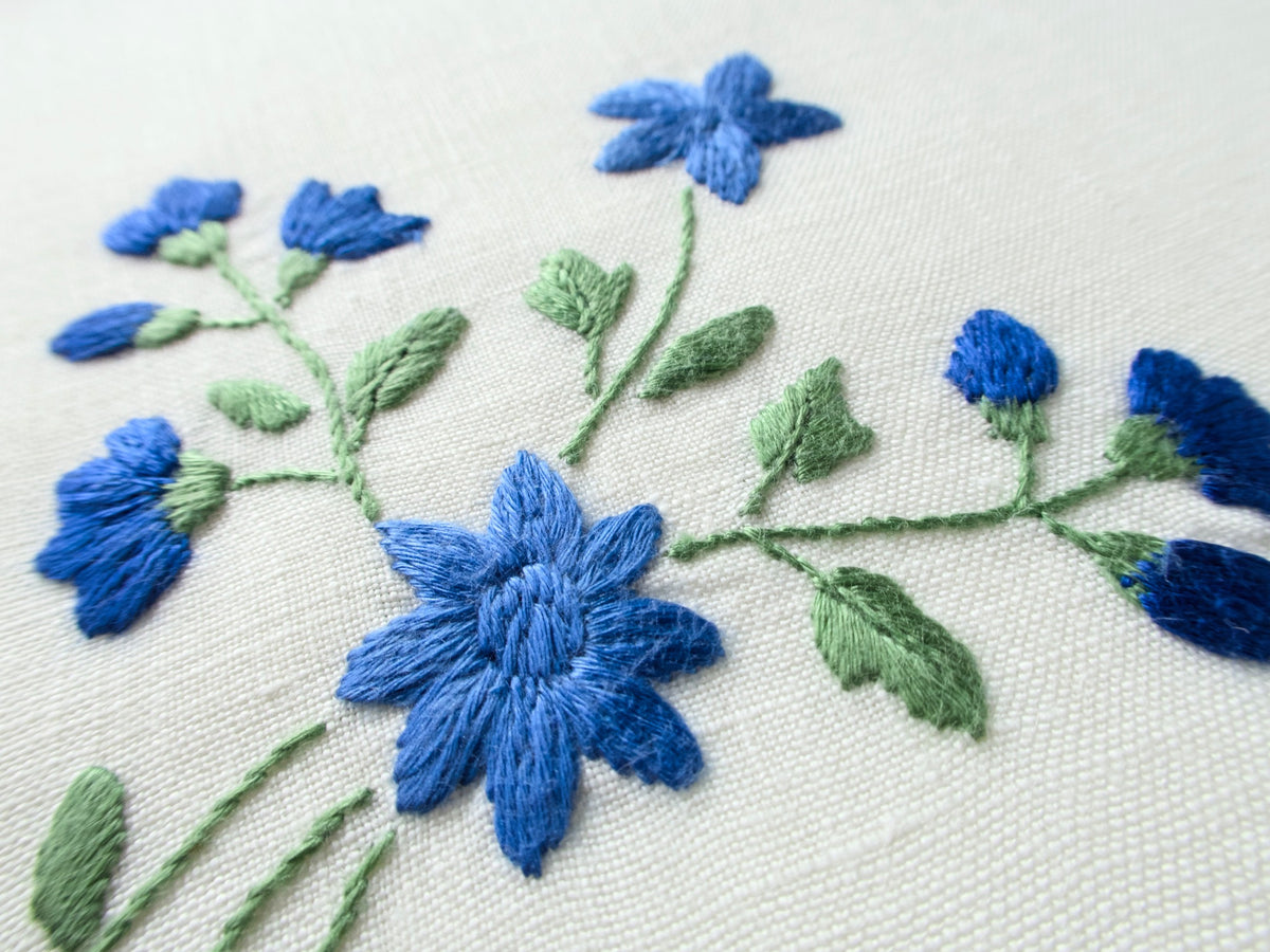 Detail from a vintage Madeira placemat showing a blue forget-me-not embroidery cluster on off-white linen