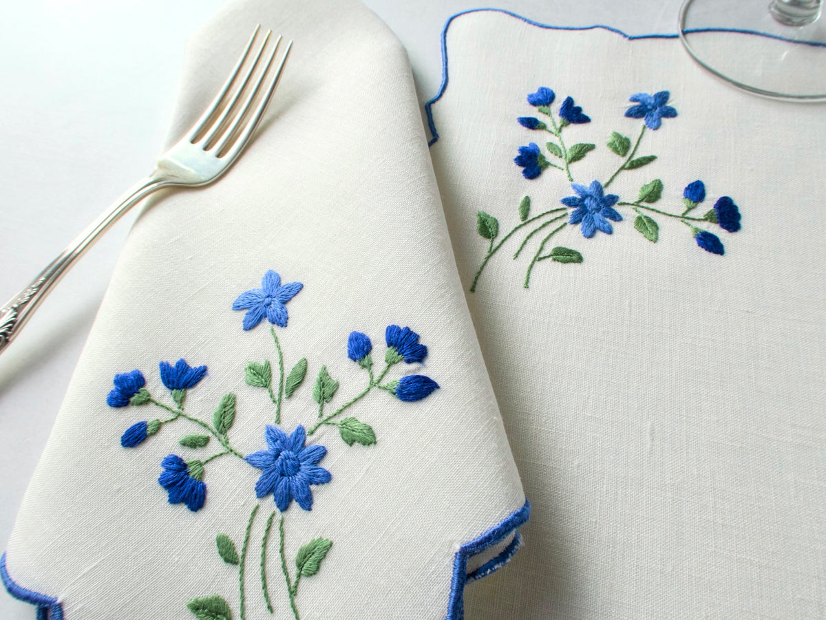 Folded vintage Madeira napkin and placemat showing blue forget-me-not embroidery and blue scalloped edge detail